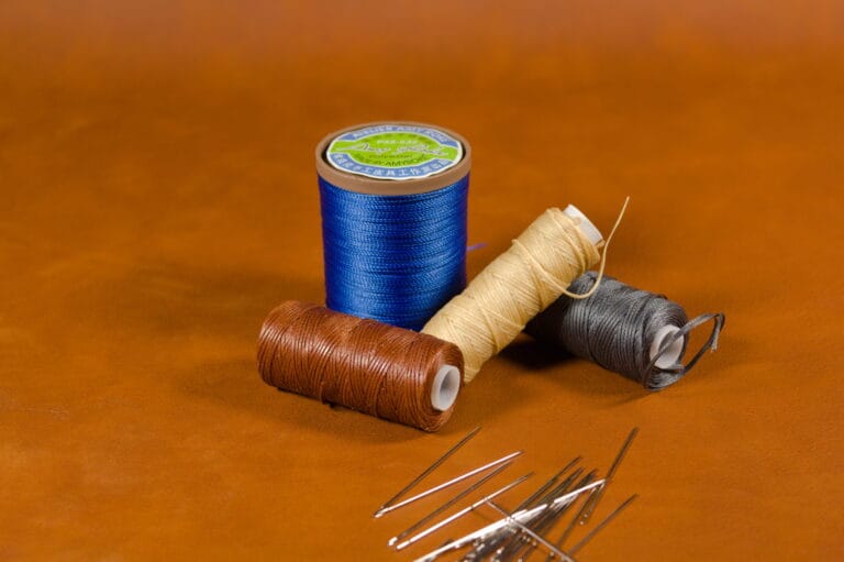 Leathercraft thread spools and stitching needles on tan leather background