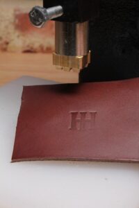 Leather logo stamp impression pressed into brown vegetable-tanned leather using an arbor press.