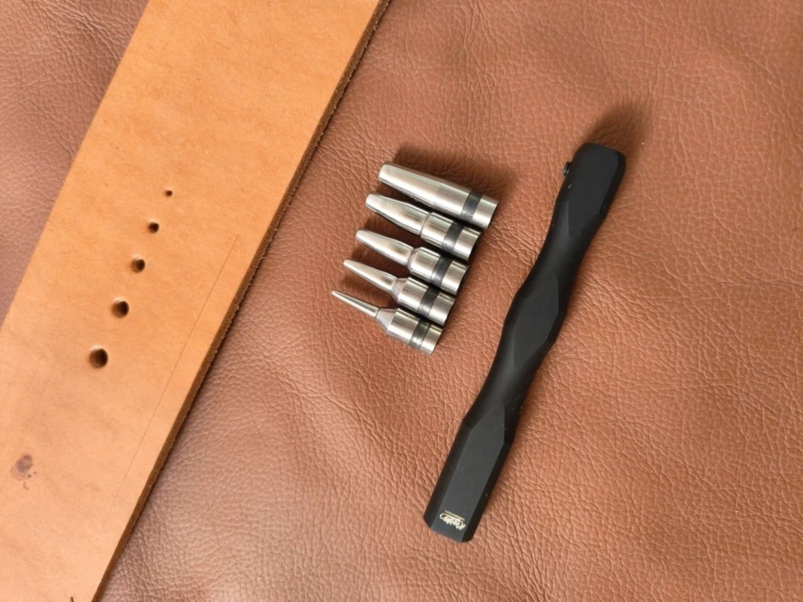 Kevin Lee interchangeable hole punch handle and tips displayed beside sample holes in leather