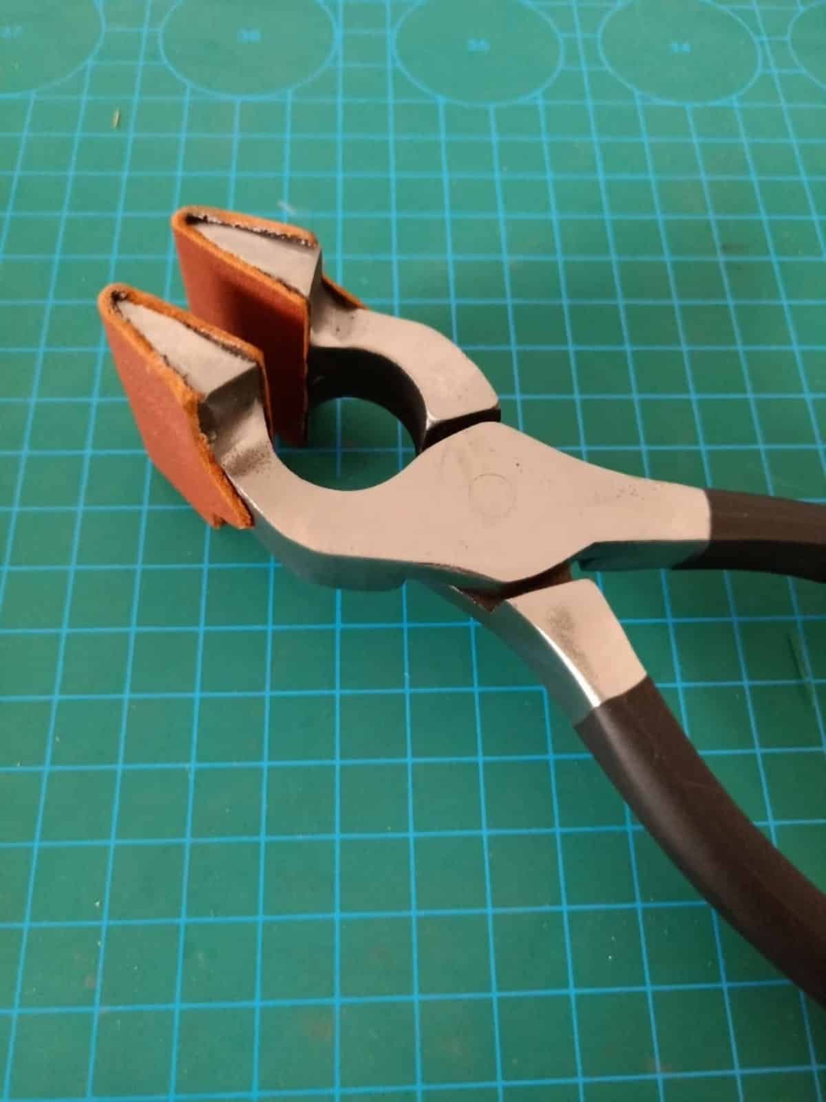 Kevin Lee steel leather edge pliers with leather-covered jaws on a gridded cutting mat