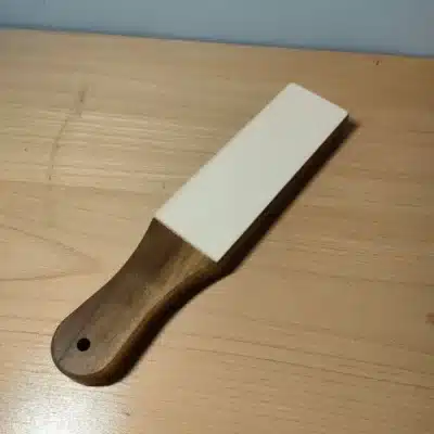 Kevin Lee black walnut strop with a white stropping surface and a handle with a hanging hole