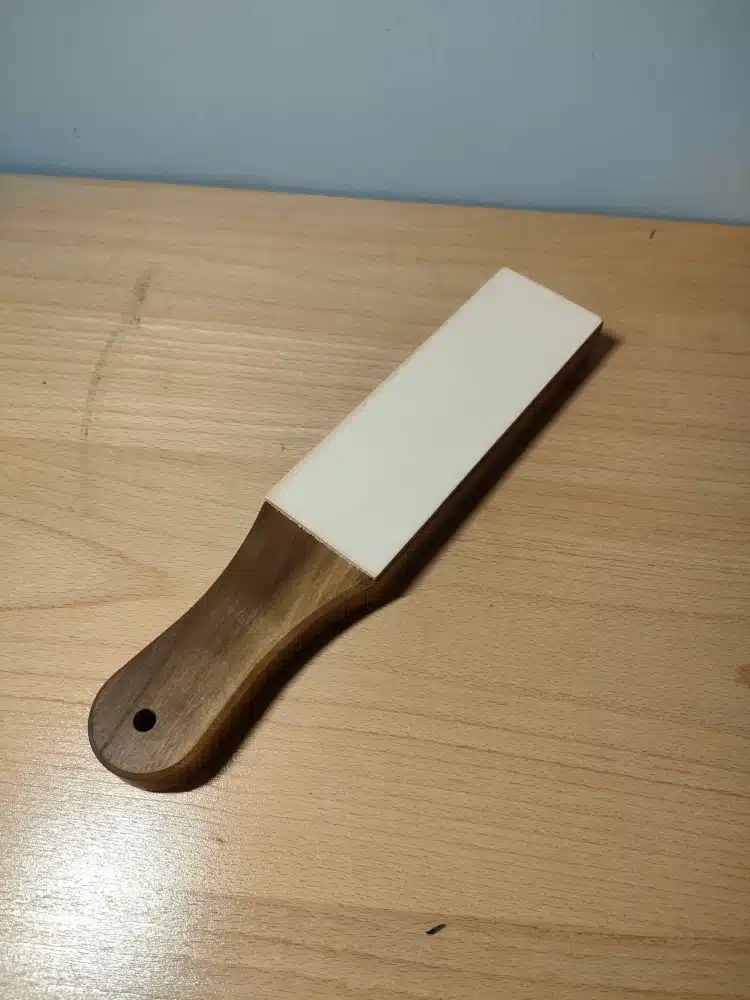 Kevin Lee black walnut strop with a white stropping surface and a handle with a hanging hole