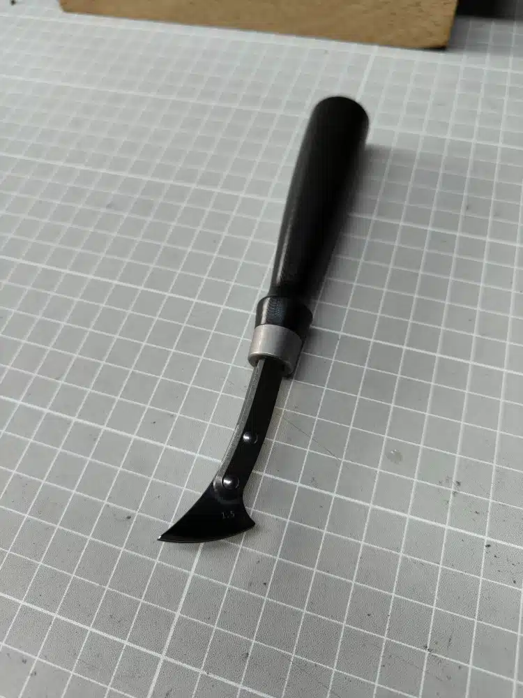 Kevin Lee G10-handle fixed creaser with a black handle, silver-coloured collar and riveted head marked 1.5, on a cutting mat