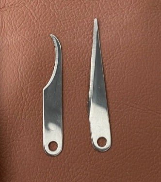 Two replacement blades, one hooked and one straight pointed, each with a mounting hole, on brown leather
